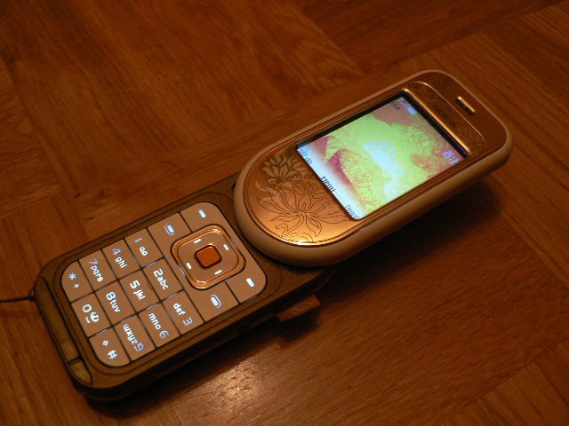 Il Nokia 7370 aperto, con la tastiera scoperta dalla rotazione e un disegno floreale inciso sulla scocca color ambra.