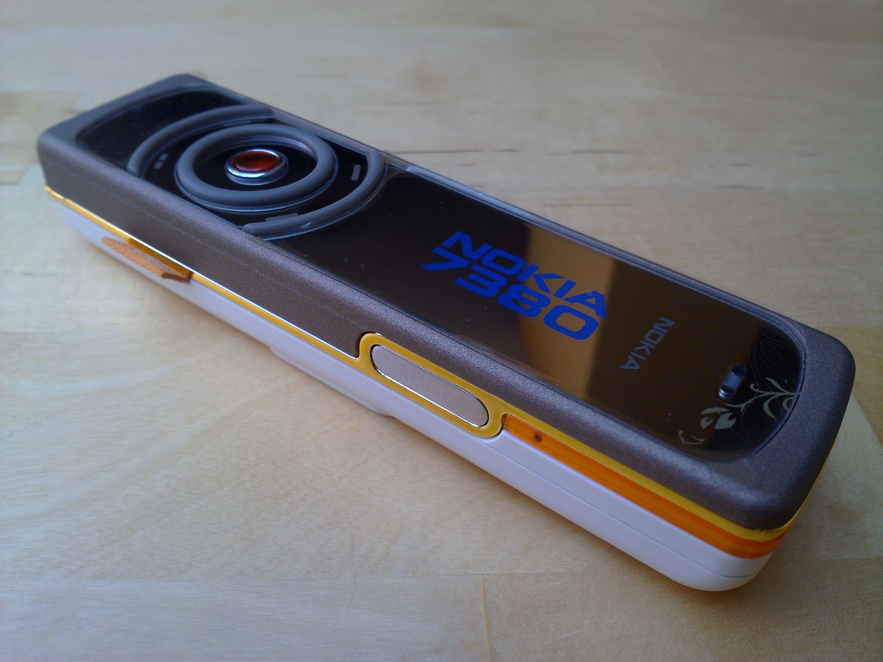 Il Nokia 7380 su un tavolo di legno: forma allungata, superficie a specchio, una ghiera circolare al posto della tastiera.